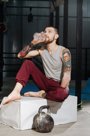 Thirsty armless young man drinking water on a pedestal next to a kettlebellの写真素材