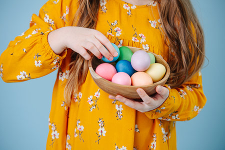 Little girl holding plate with easter eggs over blueの写真素材