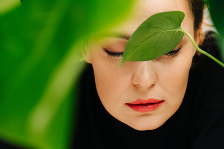 Sensual girl with beautiful makeup and red lips among green leavesの写真素材