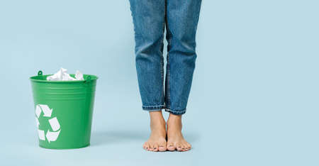 Bare feet in jeans and a green bucket with paper
