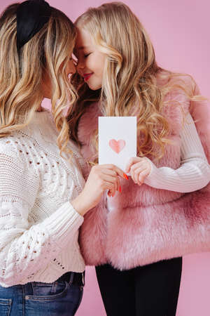 Daughter gives her mother a card with a heart on a pink background