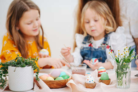 Two little daughters painting easter eggs behind a tableの写真素材