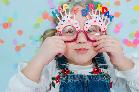 Happy little girl lies on a floor, holding onto her birthday glassesの写真素材