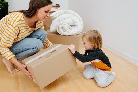 Toddler helps mom open a box after moving into a new homeの写真素材