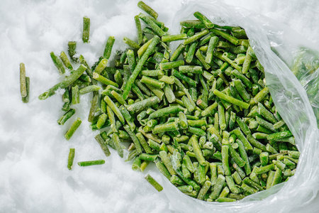 Sliced frozen green beans spilled from plastic bag on a grinded ice. top view.