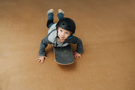 Adorable little boy lying on a skateboard, looking up at the cameraの写真素材