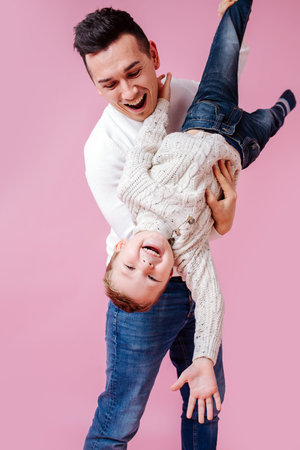 Loving euphoric dad holding cheerful son in hands upside down, playing