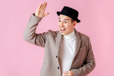 Saluting man dressed in a coat and a classical porkpie hat waving his handの写真素材