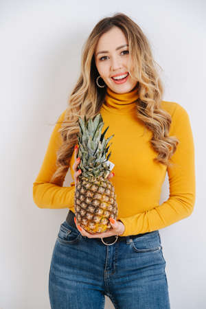 Cheerful beautiful woman in bright yellow long-sleeve with pineappe in hand