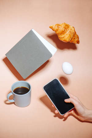 Croissant, egg and notebook hovering in air. Hand taking picture on a phone.の写真素材