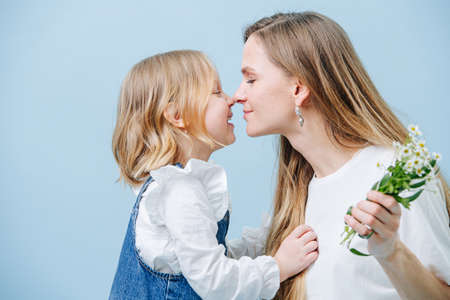 Little girl receives a hug from her mother for giving bouquet of wild camomilesの写真素材