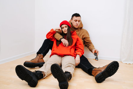 Young man and woman cuddling, sitting on the floor in hoodies and army boots