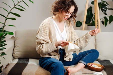 Excited young woman sewing in comforts of her apartment, embroiders a pictureの写真素材