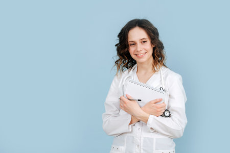 Realxed happy thoughtful female nurse standing with a notebook in her hands. Over blue background....
