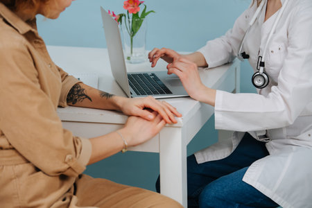 Patient in a doctor's office, waiting for her to type in a patient's history. Over blue background. She wears white robe, jeans and stethoscope.の写真素材