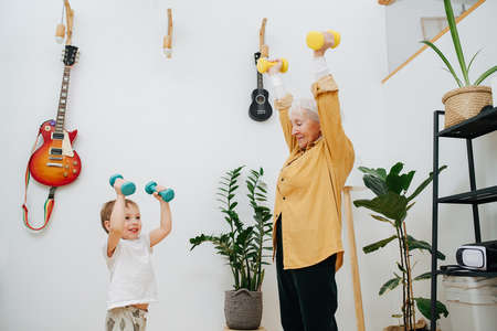 Senior woman and her young grandson together do exercises by lifting dumbbells up. High quality photoの写真素材
