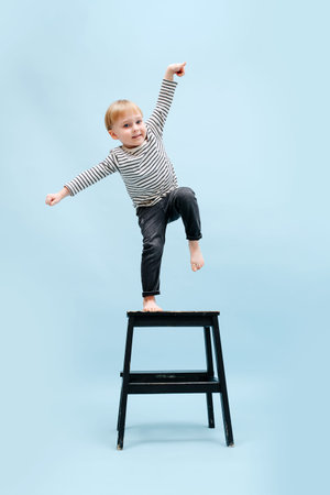 Agile barefoot blond boy balancing on one foot on a stepping stool, tilting to the side. He's...