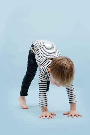 Flexible blond boy standing on all fours with straight legs. He's wearing striped long-sleeve shirt....