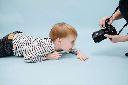Cameraman capturing grinning little blond boy lying on the floor. Studio shot.の写真素材