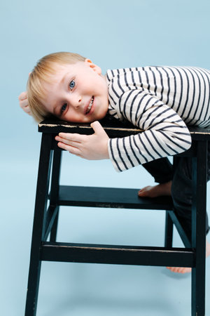 Cute blond boy lying on a stepping stool, relaxing Over blue backgroundの写真素材