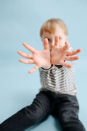 Blond boy sitting on the floor, holding joined wrists close to the cameraの写真素材