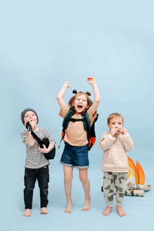 Noisy children standing next to a fake campfire with paper flames and birch logs. They are being loud and naughty, fooling around. Over blue background.の写真素材