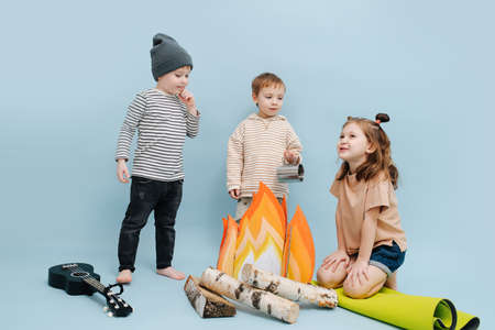 Attentive boys listening to little girl's story next to a fake campfire with paper flames and birch logs. They are acting scene, gathering over blue background. Boys looking at the girl.の写真素材