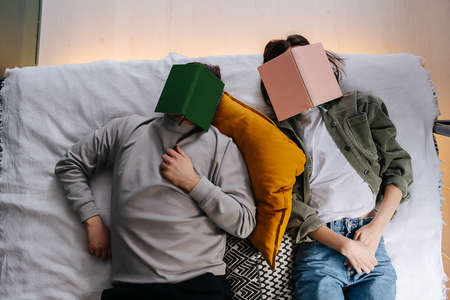 Cute funny couple napping with face covered with a book. Top view. Wearing casual daily clothes.の写真素材