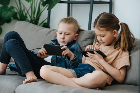 Little siblings sitting on the couch, watching their phones next to each other