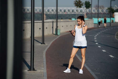 Beautiful athletic woman running on the new track outdoors. On a sunny day under a clear blue sky. She is wearing white sleeveless shirt and mini shorts.の写真素材