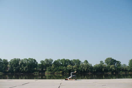 Long shot of a woman doing yoga on the pavement on a riverside