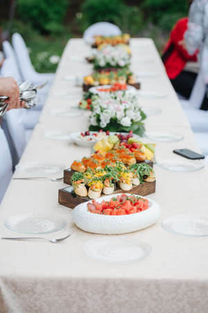 Big dining table outdoors, abundant in the food, ready for guests. Dishes layed in a straight line on a thick wooden boards and plates.の写真素材