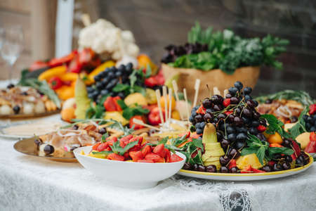 Abandant table set for an event. Large plates full of carved fruit and canapes. Low angle.