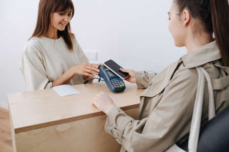 Charming young woman paying for her yoga practice in a studio to the personnel at reception stand.の写真素材