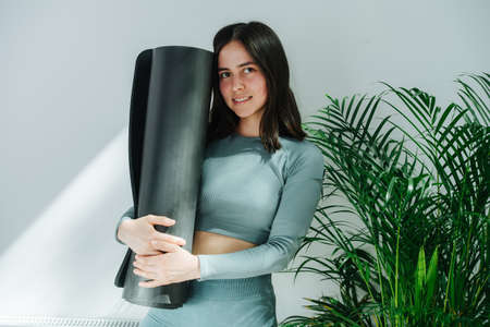 Modest young woman with subtle smile posing with a yoga mat, hugging it.