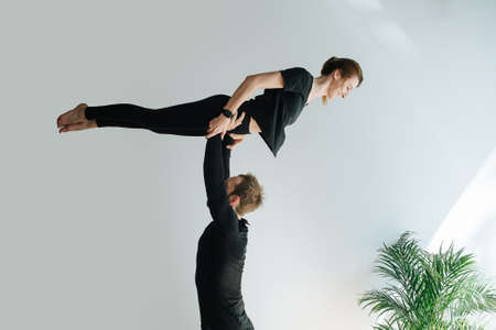 Fun couple doing gymnastic form, he is holding her on strtaight arms by the waist. She is trying to keep her body straight. In front of a white wall.の写真素材