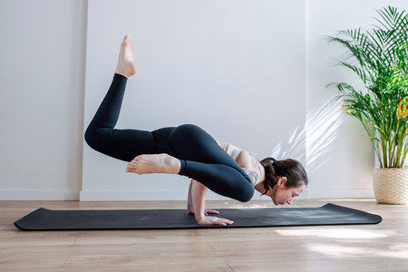 Skilled woman with shoulder tattoo practicing advansed yoga handstands in a big studio. Side view
