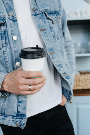 Cropped image of a man in a jeans jacket holding plastic cup of coffee. Hand in a pocket.の写真素材