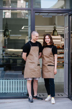 Two coworkers posing for a photo in the entrance in the transparent windowed bakery shop front. Man is socialising with his female colleague.の写真素材