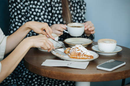 Close up image of women eating croissants and drinking coffee in a caffee. Close up, cropped, no heads.の写真素材
