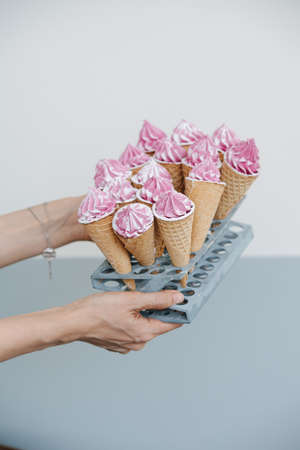 Hands presenting sweet waffle cones with pink cream on a special stand. Blurred background. Giving away. Passing.の写真素材