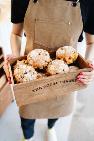 Muffins in a branded wooden box, held by a female baker in a beige apron. Cropped image, no face.の写真素材