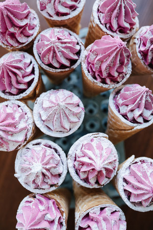 Top view on sweet waffle cones with pink cream on a special stand. Sprinkled with sugar powder.の写真素材