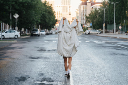 Bare legged woman wrapped in blanket walking down empty wet city road early in the morning. Playing ghost.の写真素材
