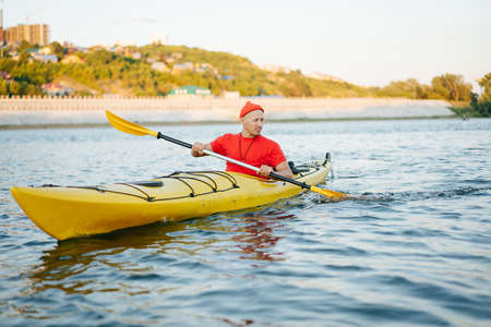 Middle aged man in orange watch cap riding on yellow kayak on a big wide river. Reinforsed...