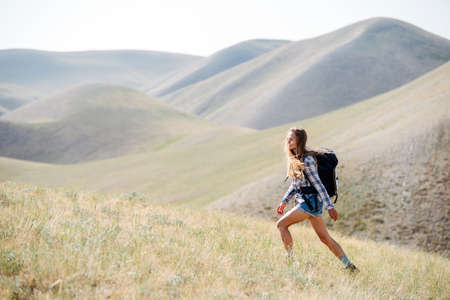 Uplifted young woman going up a slope, surrounded by a beautiful hill scenery. She's chosen quick pace, taking wide springy steps.の写真素材