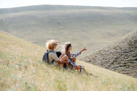 Women friends hiking in the grassy hills. Resting on the slope. Pointing finger in the distance.の写真素材