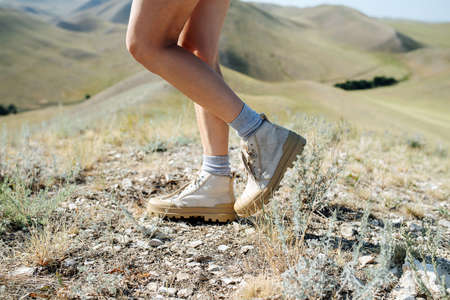 Cropped image of a woman standing on a grassy groud, enjoying hill scenery. No head. One leg lifted, bent in the knee.の写真素材