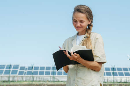 Happy smiling woman writing down things in her notepad. Over the sky view, low angle. Electric solar...