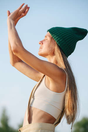 Relaxed woman in a green watch cap enjoying morning sun. Eyes closed. Side view. Bokeh.の写真素材